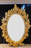 Front view of full mirror showing oval glass and ornate gilt frame