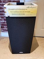 Front view of tall dark brown wicker-style planter with packaging sleeve attached