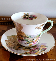 Front view of teacup on saucer showing landscape design and gilt rims