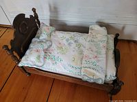 Oblique view of doll bed showing headboard, turned posts, comforter and pillow