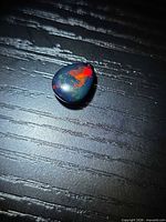 Top view of pear cabochon black opal showing vivid red and green play of color
