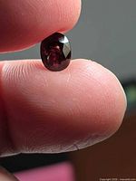 Oval deep red spinel held between fingers showing overall shape and faceting