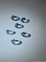 Six light blue oval faceted gemstones on neutral background