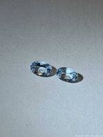 Two oval-cut light blue aquamarines on neutral background