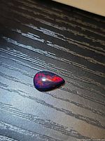 Pear-shaped black fire opal front view showing red flashes