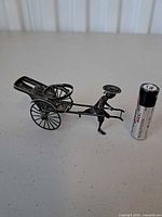 Full view of silver rickshaw and puller with battery for scale