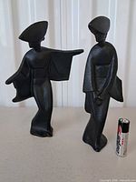 Front view of both cast iron geisha figurines with AA battery for scale