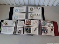 Overview of three open albums showing numerous First Day Cover envelopes in plastic sleeves