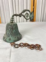 Side view of bronze bell, bracket, and chain on table