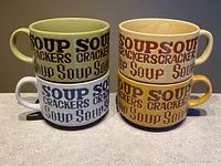 Front view of four stacked mugs showing two color variants and lettering