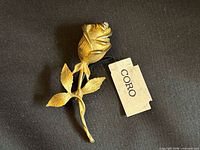 Front view of gold tone rose brooch with attached Coro tag