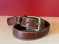 Coiled brown leather belt showing buckle, stitching and overall appearance