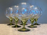 Six clear crystal snifters with green stems, front angle