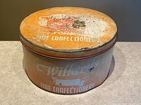 Top and side view of round litho advertising tin showing "Willard’s Fine Confectionery" text and worn surface