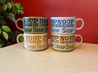 Stacked view of the four stoneware mugs showing colour variations and raised typography