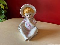 Front view of bisque porcelain figurine showing seated girl with bonnet