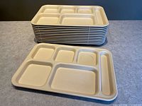 Stack of twelve beige compartment trays plus one tray laid flat showing six sections