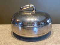 Side view of covered serving dish showing domed lid, curling stone-style handle and overall form