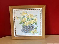 Front view of framed ceramic tile trivet featuring yellow daisies basket design