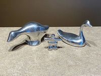 Front view of three polished aluminum sculptures: goose, Inukshuk, swan