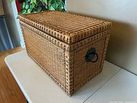 Three-quarter view of wicker chest closed showing weave and handle