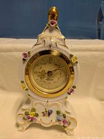 Front view of porcelain mantel clock showing dial and floral decoration