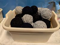 Cream bin holding multiple wool yarn balls in grey, black, navy