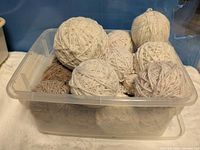 Plastic bin holding multiple cream and beige wool yarn balls