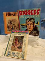 Front covers of three vintage books: Robinson Crusoe, Biggles Air Detective, Robin Hood and His Merry Men