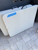 Two folded Office Star tables leaning against wall, showing carry handles