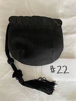 Front view of black pleated evening purse showing scalloped hard top, braided cord and tassel