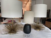Three lamps on table: two gold starburst base lamps, one small black base lamp