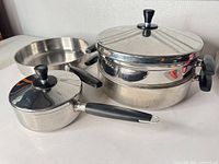 Full view of fry pan, saucepan with lid, stacking pot with lid and side handles