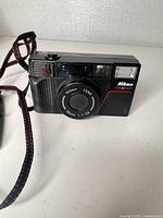 Front view of Nikon One Touch camera showing lens, flash, branding, and attached strap