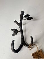 Front view of cast iron wall hook with leaves and tag