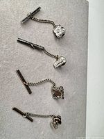 Overview of four silver-tone tie tack sets with chains and bars