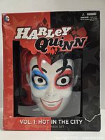 Front of boxed set showing Harley Quinn mask through window and title text