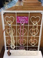 Full front view of the white metal frame featuring several necklaces hung on the heart-shaped hooks within the grid structure.