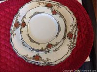 Stacked dinnerware showing dinner plates, luncheon plates, salad plates with scalloped edges, floral and vine pattern in orange, gold and black trim.