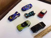 Top view of six toy cars showing colors and designs including a blue racing car, stock car number 5, classic Mini Cooper, green convertible, black sports car, and vintage open-top car.