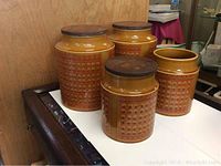 Four yellow/orange ceramic canisters with circular geometric patterns and wood lids, lined up on a white surface, photographed from an angle.