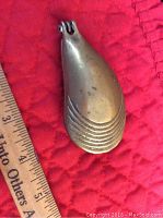 Image showing closed brass oyster-shaped holder approximately 3 inches long on red quilted background with ruler for size reference.