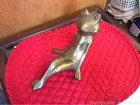 Front view of large brass frog figurine sitting on a red quilted mat showing upright sitting pose and smooth finish.
