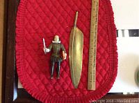 Shakespeare figurine and feather-shaped pen arranged next to a ruler for size reference, showing the front of the figurine and pen.
