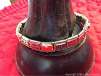 Side view of the silver-tone link bracelet showing the red heart link with 'family' and other engraved metal links with faith/family messages.