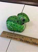 Side view of green tin turtle toy with ruler for scale showing about 3.5 inches long.