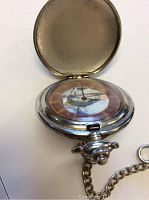 Pocket watch open showing bass fishing motif on dial, silver-tone protective case interior visible.