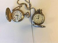Two silver-tone pocket watches opened to show faces, one with chain, one with engraved designs.