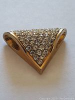 Front view of gold-toned triangular pendant covered in clear rhinestones arranged in rows.