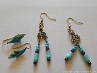 Photo showing two pairs of earrings, one with dangling turquoise beads and metal scrollwork, the other shaped like turquoise feathers.